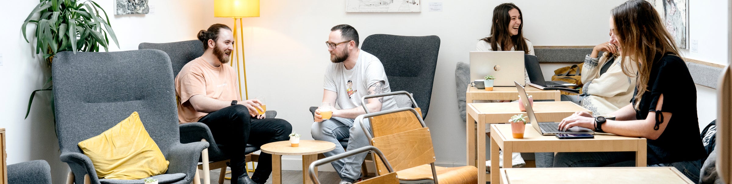 Inside Coffee + Beer: customers chatting in grey armchairs and working at pine tables